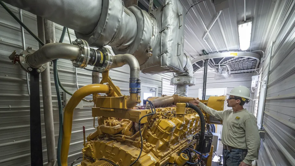 A technician in a hard hat checking a large industrial engine