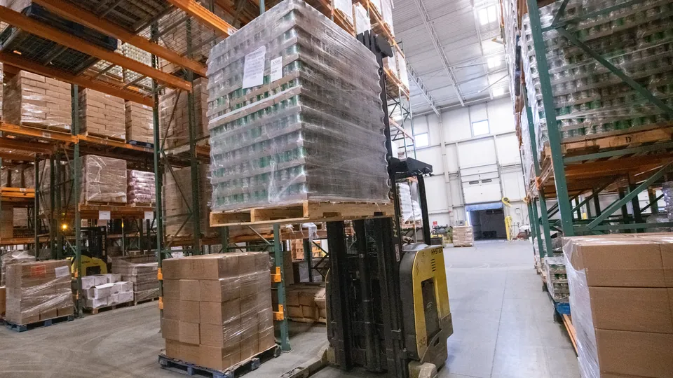 A reach truck lifting a shrink-wrapped pallet into high-bay racking in a distribution centre